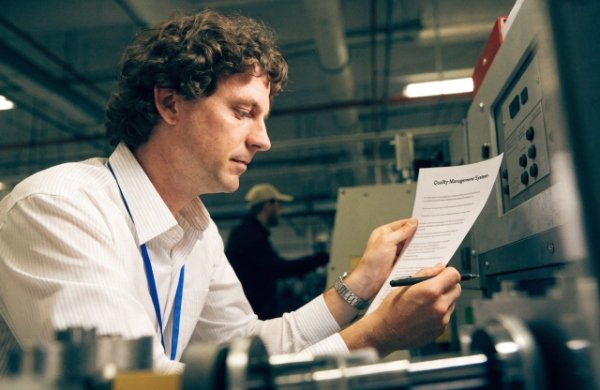 ISO 9001 Quality Management System An auditor reviewing a quality management system document in a factory setting